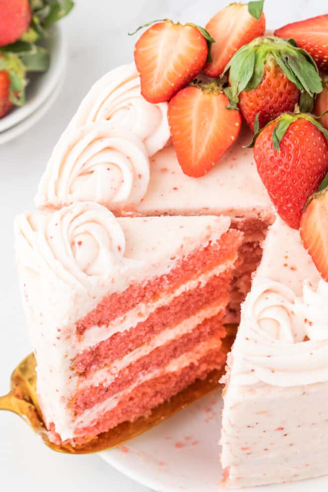 strawberry layer cake with a slice being removed so that you can see the four layers inside 