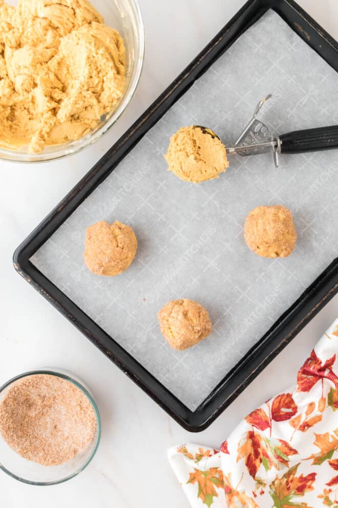 Baking Pan lined with parchment with a cookie scoop and scoops of cookie dough on the pan