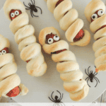 Mummy Dogs - hot dogs wrapped in homemade dough, baked to a golden brown and edible eyes attached on white platter with text overlay