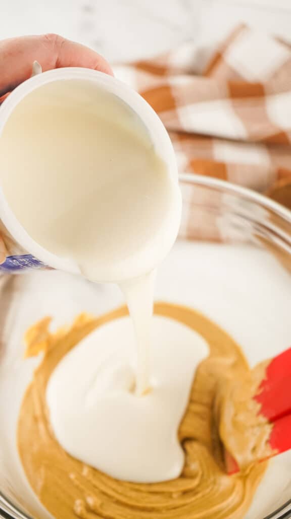 melted canned frosting being poured into bowl of melted peanut butter chips