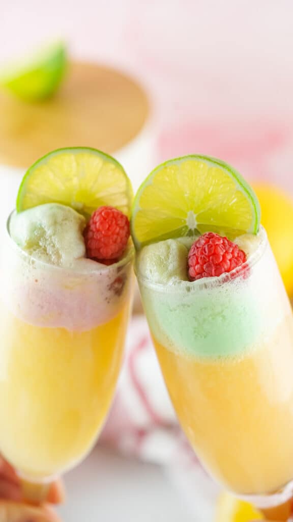 toasting flutes filled with sparkling apple cider floats topped with lemon and lime slices and a raspberry