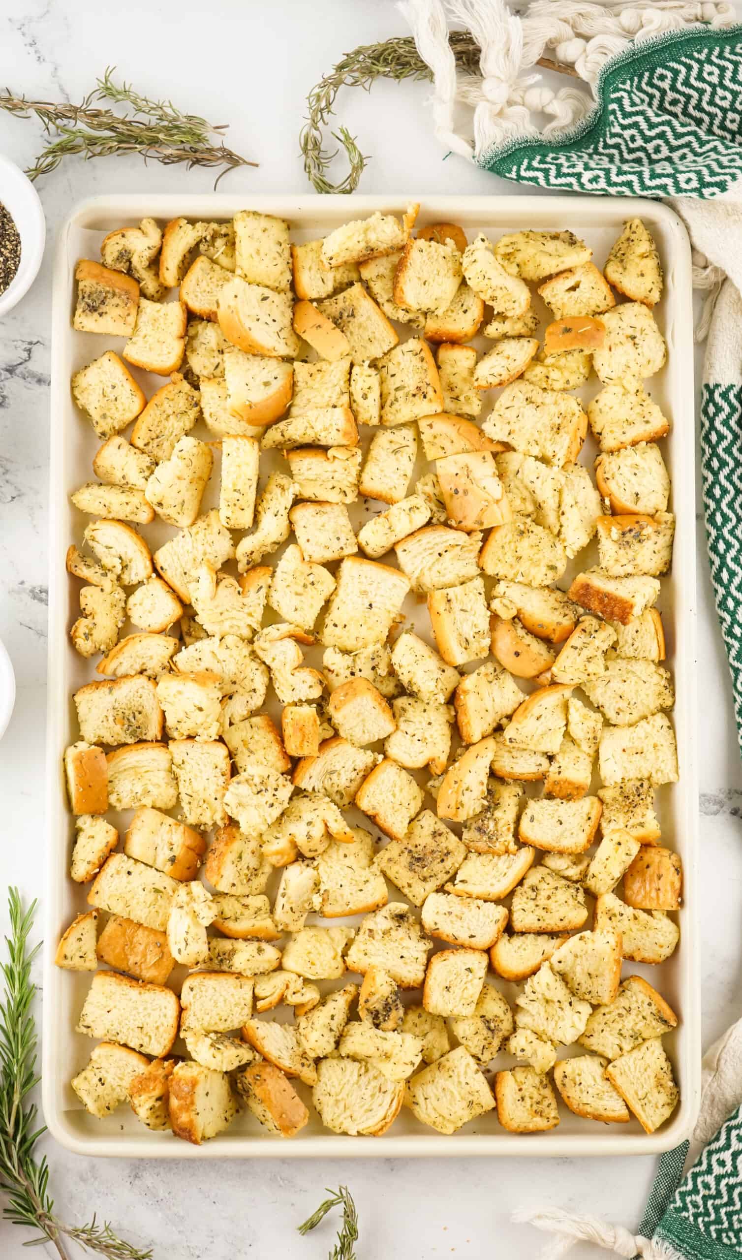 seasoned bread cubes spread on a baking sheet ready to bake