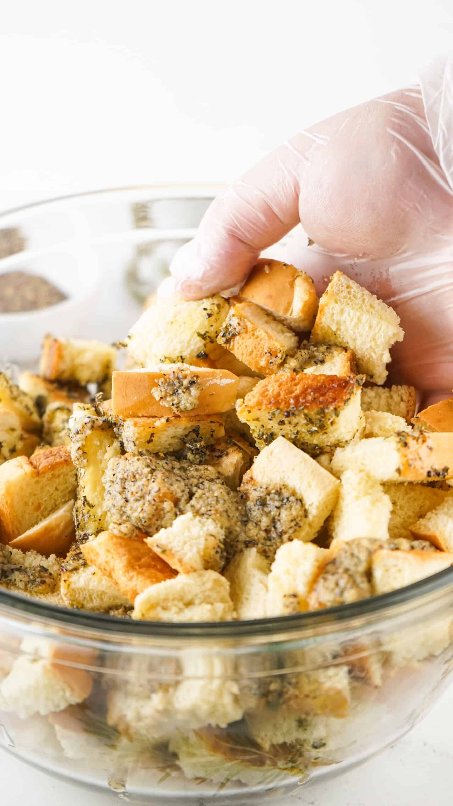 a gloved hand mixing seasonings and bread cubes together before baking croutons