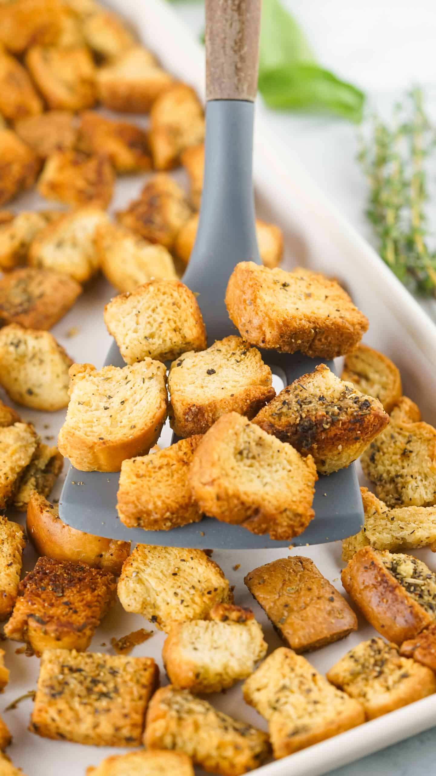 scooping golden brown baked Italian Seasoned Croutons from baking sheet