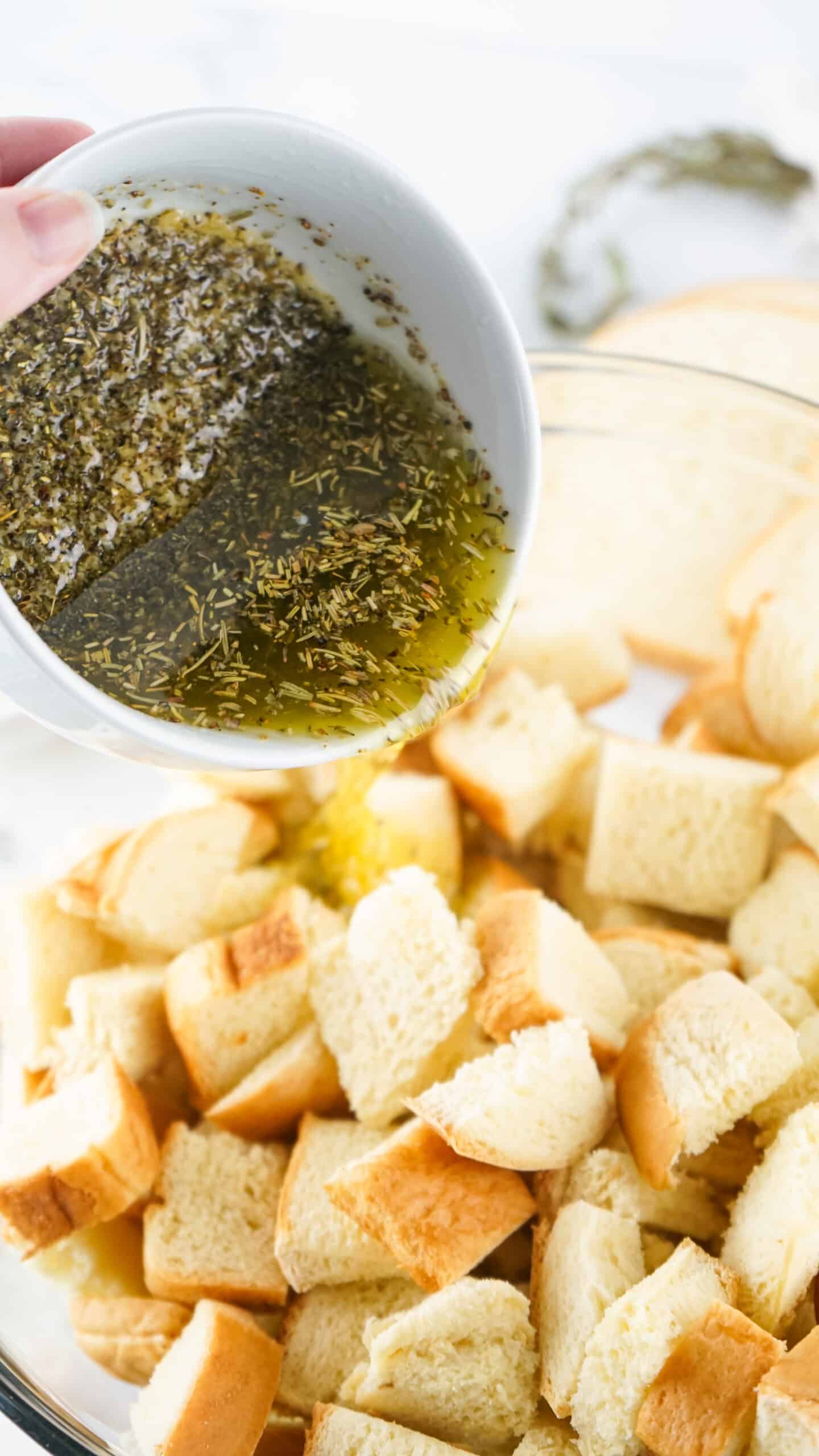 melted butter and seasonings being poured over cubed bread for homemade croutons