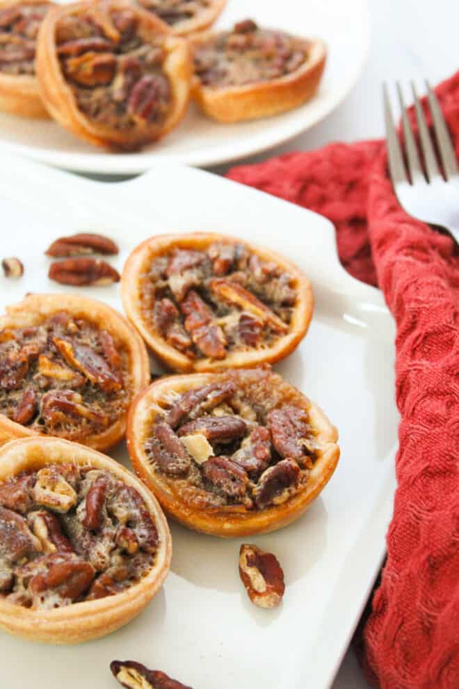 Little pecan pies on a white serving dish with a red cloth over to the side