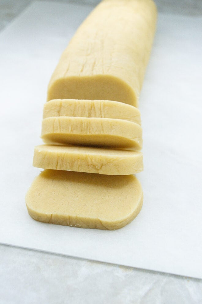 chilled sugar cookie log being cut into slices before baking