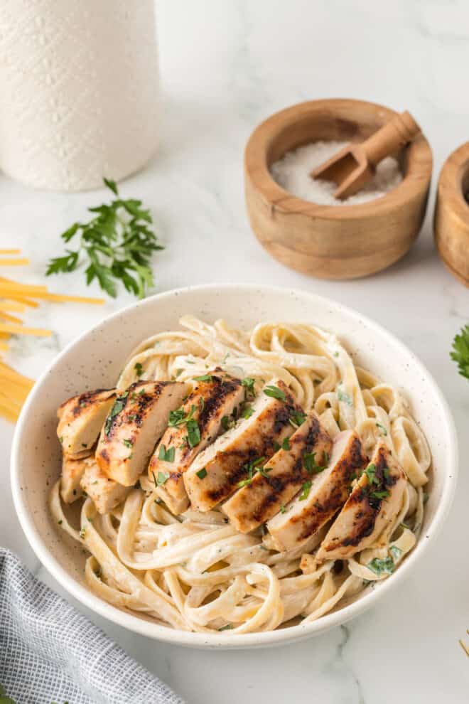 Grilled Chicken breast sliced and placed on top of fettuccine Alfredo in a white serving plate with a rim