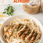 White bowl filled with fettuccine Alfredo and topped with slices of grilled chicken