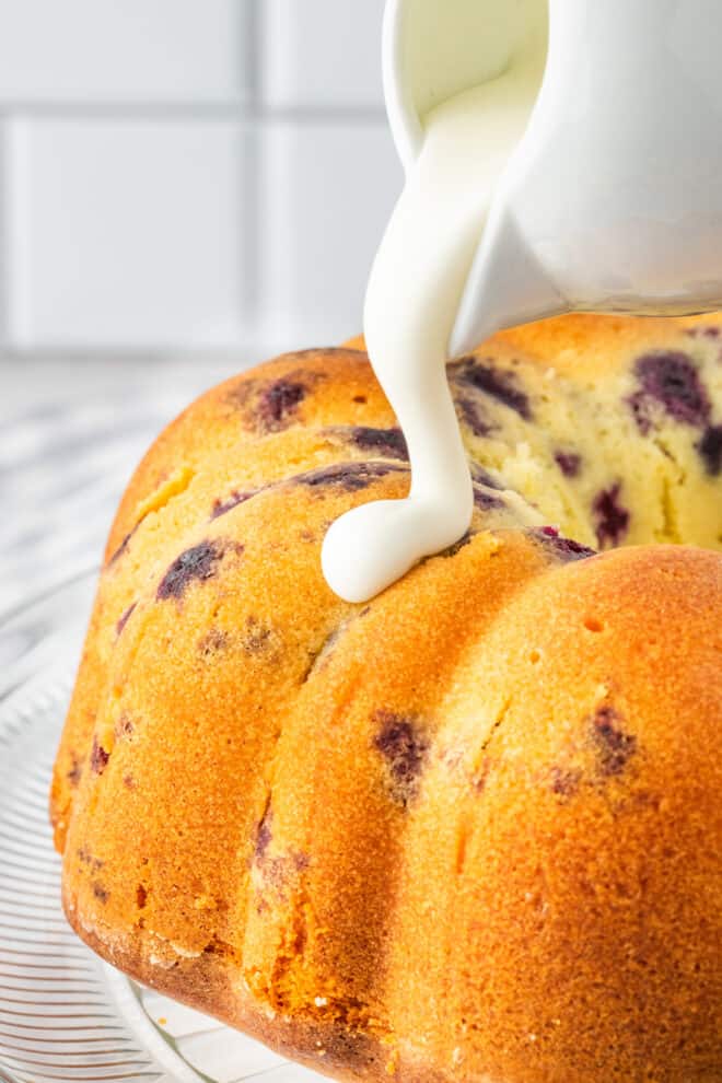 Glaze being poured over the top of lemon blueberry cake