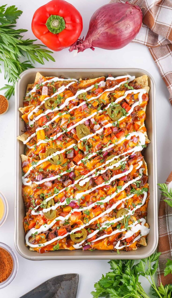 sheet pan with pulled pork nachos drizzled with sour cream and BBQ sauce