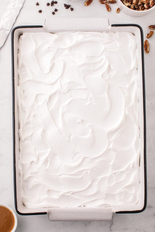 whipped topping spread over chocolate turtle poke cake
