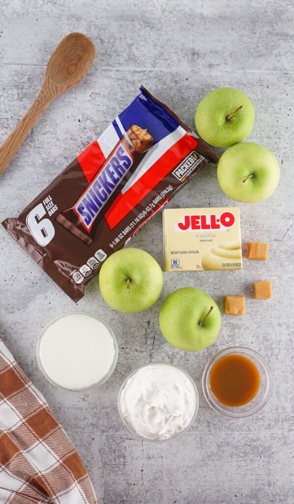 ingredients to make Snickers Salad including apples, Snicker bars, instant vanilla pudding and caramel sauce