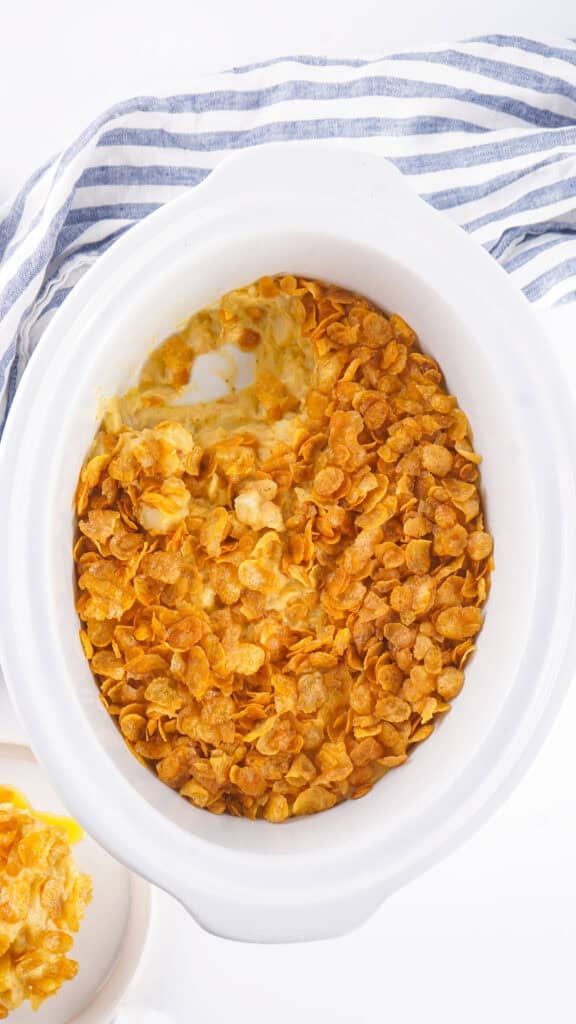 slow cooker with a cheesy hash brown casserole topped with crispy cornflakes