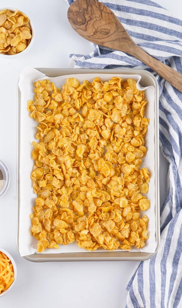 butter covered cornflakes on a parchment lined baking dish before baking in the oven