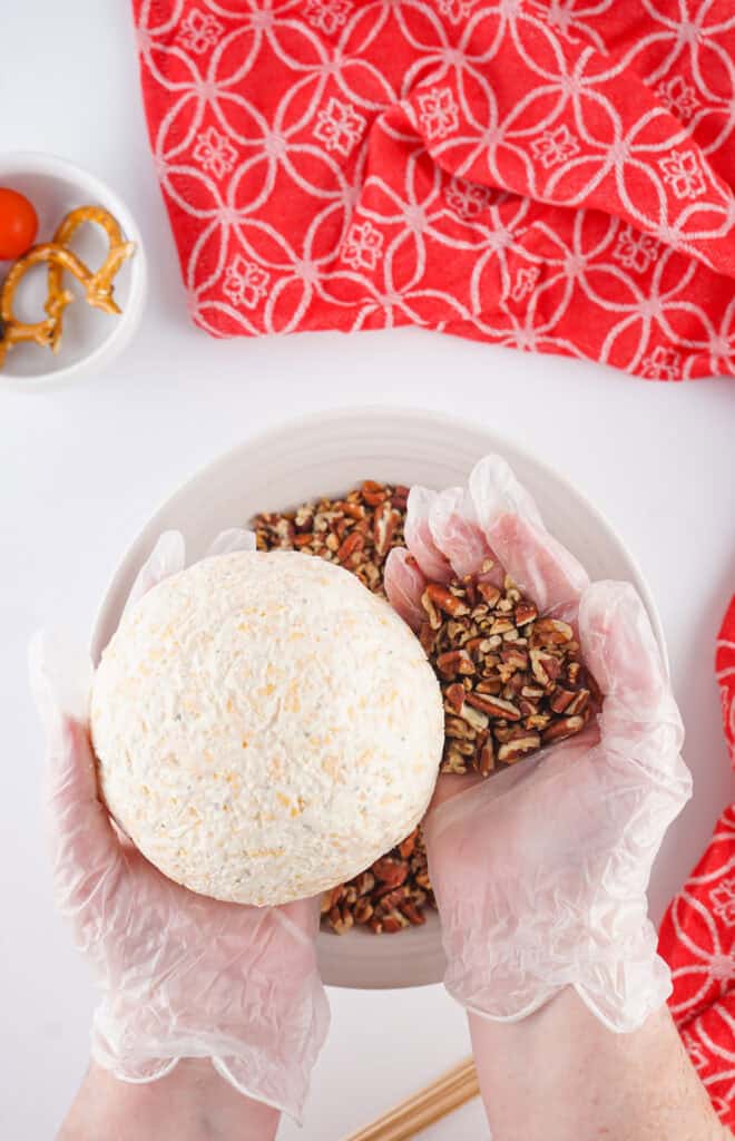 cheeseball being coated in chopped pecans