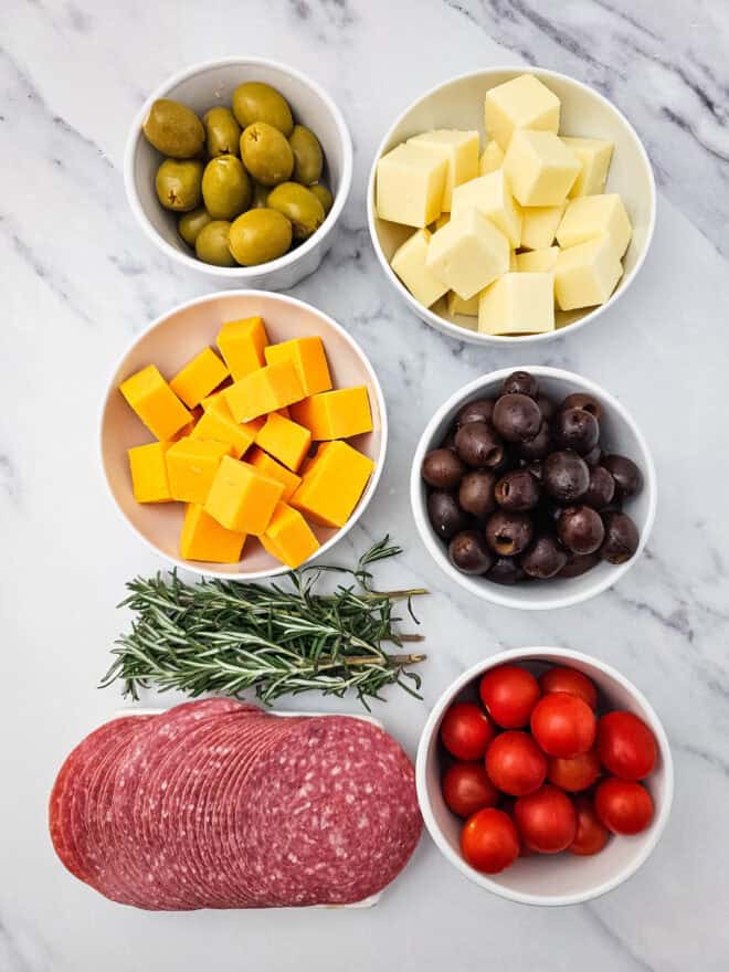 Ingredients for charcuterie wreath - cheese cubes, olives, tomatoes, salami and rosemary sprigs