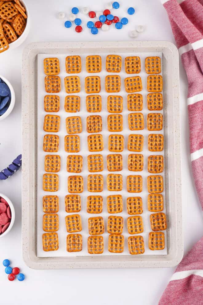 pretzel bites lined up on a 9x13 pan ready to be topped with candy melts before baking