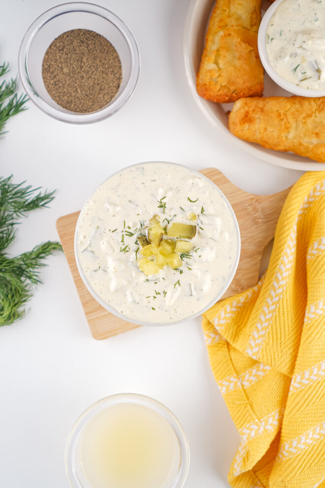 Overhead view of tartar sauce in a white bowl with fish sticks in the background