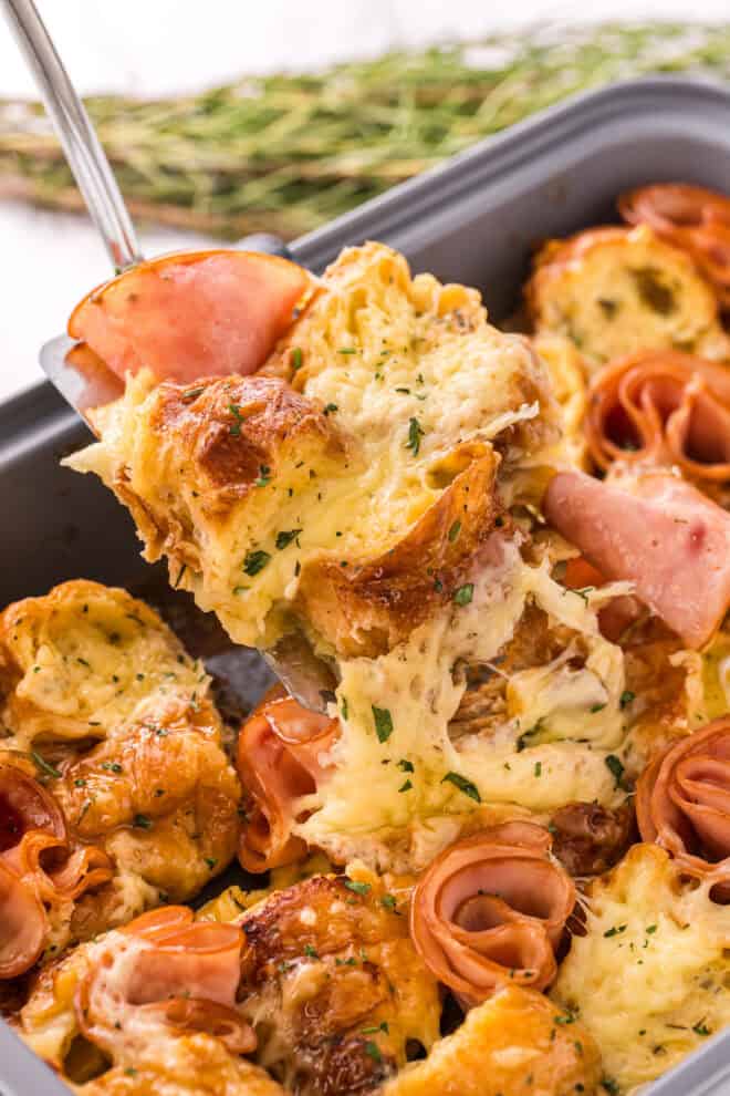 A serving of ham and cheese croisssant bake being removed from the baking pan