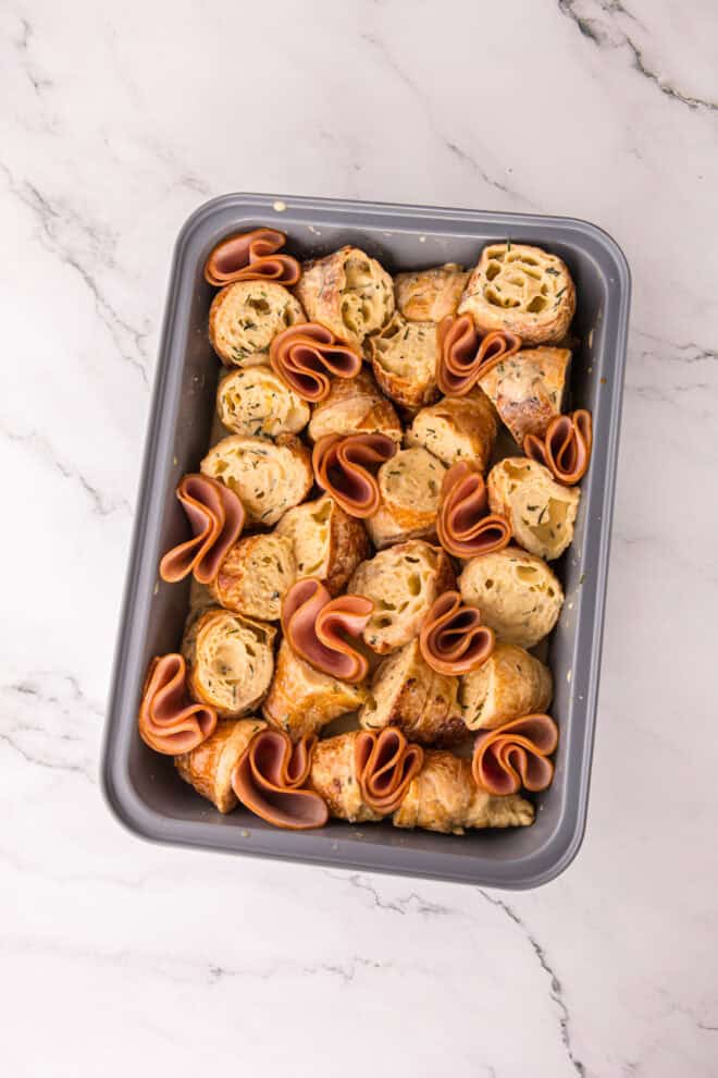 slices of ham nestled into the croissant pieces in casserole dish