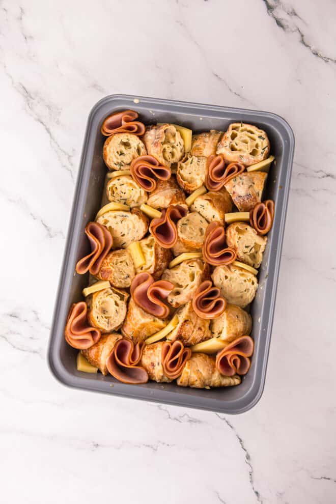 slices of cheese tucked in between the ham slices and croissant pieces in casserole